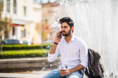 Çeşme oturan ve sokakta telefonda konuşurken yakışıklı genç Hintli adam