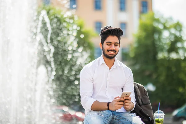 Jonge Indiase Man Zittend Straat Kijk Telefoon Achtergrond Van Fonteinen — Stockfoto