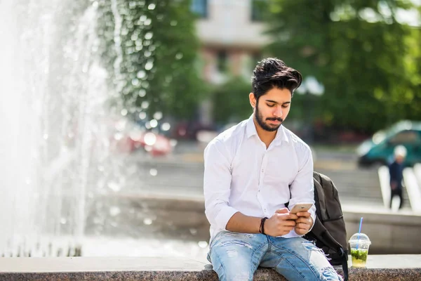 Jonge Indiase Man Zittend Straat Kijk Telefoon Achtergrond Van Fonteinen — Stockfoto