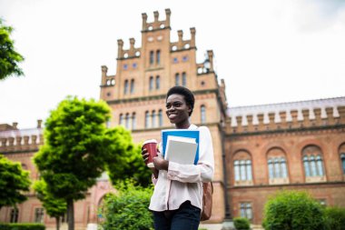 Eğitim, teknoloji ve insan kavramı - gülümseyen kadın Afrikalı-Amerikalı öğrenci ile çanta ve take away kahve fincanı