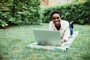 Laptop Kampüsü'ndeki çalışma çim üzerinde yalan Afro Amerikalı üniversite öğrencisi