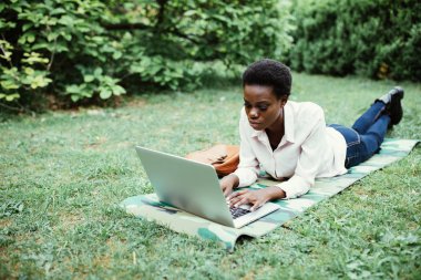 Laptop Kampüsü'ndeki çalışma çim üzerinde yalan Afro Amerikalı üniversite öğrencisi