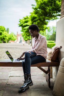 Derin düşüncelere sınava hazırlanıyor kampüste bir dizüstü bilgisayar üzerinde çalışan bir bankta otururken arayan genç Afrika Bayan üniversite öğrenci odaklı