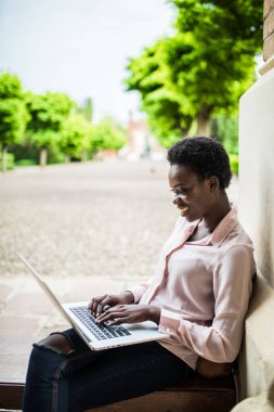 Derin düşüncelere sınava hazırlanıyor kampüste bir dizüstü bilgisayar üzerinde çalışan bir bankta otururken arayan genç Afrika Bayan üniversite öğrenci odaklı
