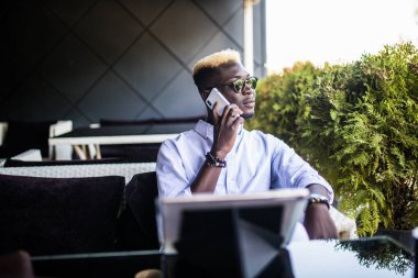 Bir kafede otururken cep telefonuyla konuşan gülümseyen adam portresi