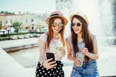 Memnun iki karma yarış bayanlar fotoğrafını cep telefonu üzerinde iyi haber almak, e-posta veya selfie akıllı telefon ile yapmak, açık havada taze kokteyl içmek. Irklararası arkadaşlık ve eğlence zaman kavramı