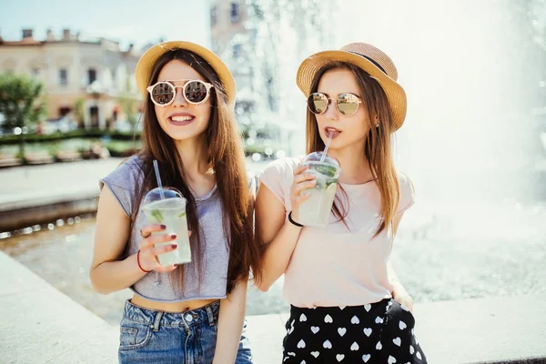 两个美丽的年轻女孩在夏天阳光明媚的城市喝鸡尾酒 — 图库照片