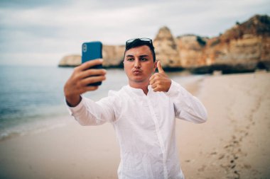 Mutlu genç adam denizde tatil sırasında cep telefonuyla selfie alarak