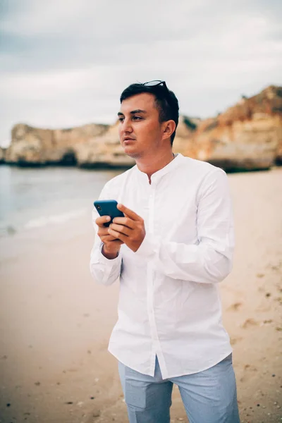 若い男が日没時に海の崖の上に携帯電話の使用 — ストック写真
