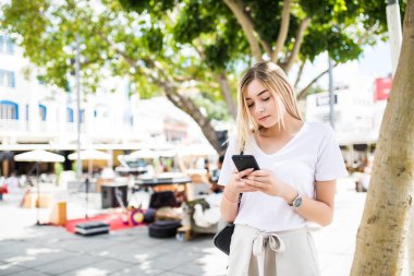 Yürüyüş ve bir akıllı telefon sokakta bir güneşli yaz günde kullanarak kadın