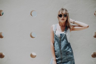 Güneş gözlüğü ve kot elbise şık güzel kadın karşı şehir duvara yaslandı