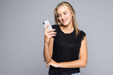 Gülümseyen ve gri arka plan karşı dururken akıllı telefonu kullanarak çekici genç kadın