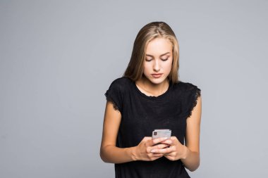 Gülümseyen ve gri arka plan karşı dururken akıllı telefonu kullanarak çekici genç kadın