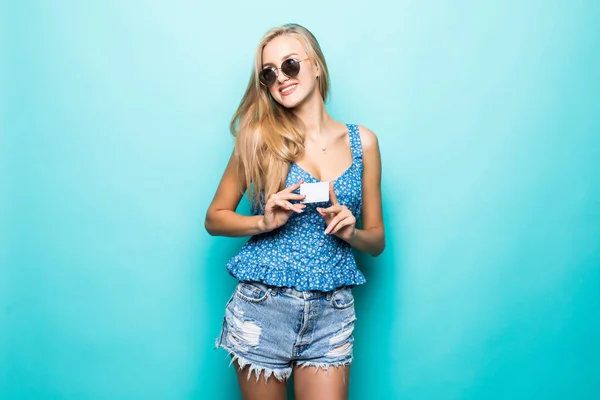 一个漂亮的年轻女子的肖像穿着毛衣指着信用卡孤立的蓝色背景 — 图库照片