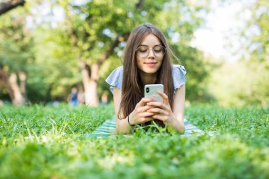 Genç güzel kadın bir cep telefonuyla mesaj okuma çim üzerinde yalan