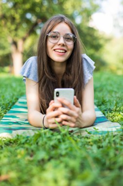 Parkta çim üzerinde yalan ve smartphone kullanarak gözlük memnun esmer kadın