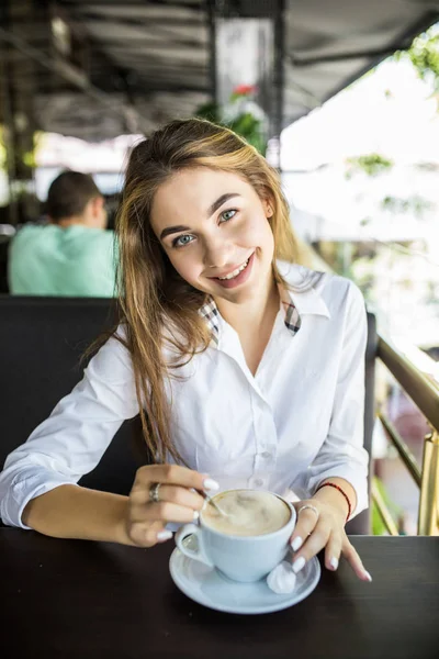 portrait of beautiful charming woman is stirring coffee in outdoor cafe and thinking