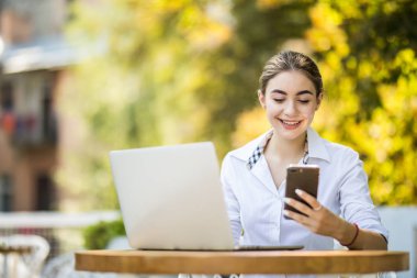 Kahve dükkanı açık havada ve kullanımları smartphone tabloda Tablo fincan kahve ve defter üzerinde oturan genç iş kadını