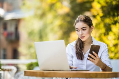 Kafede dizüstü bilgisayar ve akıllı telefon kullanan mutlu kadın görüntüsü. Bir kafede otururken ve bilgisayarda çalışan genç güzel kız