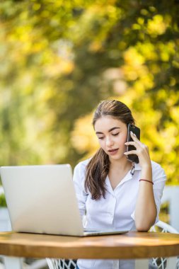 Masada oturan ve kafede telefonla konuşan mutlu iş kadını. Uzaklara bakıyorum.