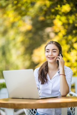 Meşgul işkadını üstünde hareket eden telefon ile laptop kafeterya masada oturan konuşuyor