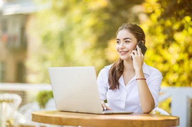 Masada oturan ve kafede telefonla konuşan mutlu iş kadını. Uzaklara bakıyorum.