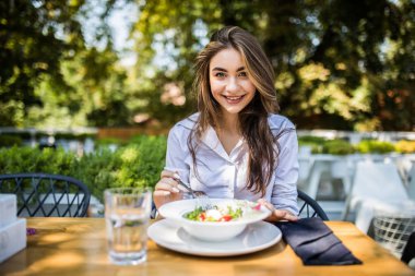 Genç kadın cafede karışık sebze salatası yiyor