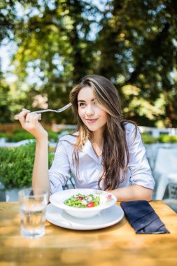 Genç kadın cafede karışık sebze salatası yiyor