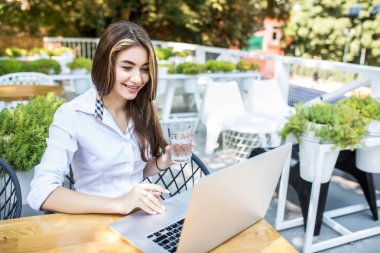 Güzel kız içme suyu restoranda. Güzel kız beyaz gömlekli laptopunu kafede üzerinde çalışıyor. Portre Bayan el Café bilgisayarda yazarak