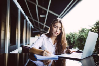 Gülümseyen kadın kafede dizüstü kullanarak ve bazı verileri Not defteri üzerinde Not
