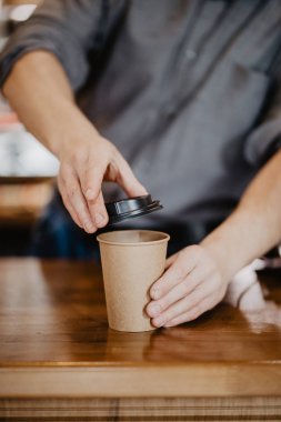 Barista önlük beyaz paket servisi olan restoran kağıt bardak eller sıcak kapuçino tutuyor. Kahve Cafe dükkanında götürün