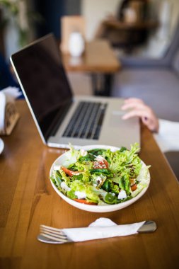 Bir kafede dizüstü bilgisayar ile oturma ve heathty salata masada yemek genç kadın.