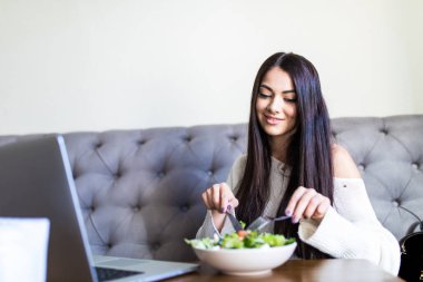 Bir kafede bir dizüstü bilgisayar ile oturma ve yemek kahvaltı genç kadın