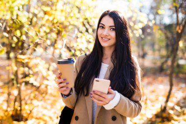 Güzel kadın açık havada, sonbahar ceket giymiş kahve içme, istimal hareket eden telefon