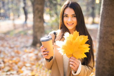 Güzel kadın içme kahve altında sonbahar park yeşillik düşmek. Altın Sonbahar park