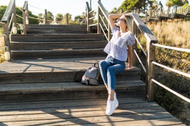 Young woman standing on the wooden stairs that going to the ocean beach clipart