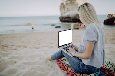 Kum kumlu plaj arka plan deniz, mavi gökyüzü ve cennet manzara üzerinde oturan dizüstü arkasında çalışan kadın serbest meslek.