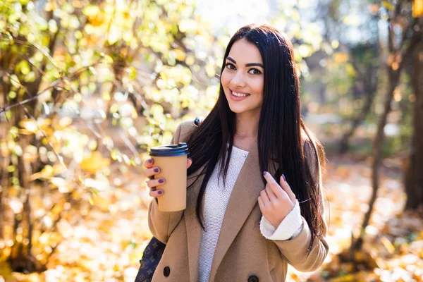 Fall woman drinking coffee in autumn city park. Girl enjoying hot drink from disposable coffee cup.