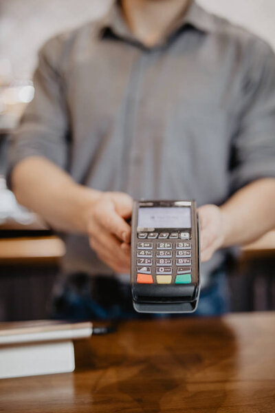 Customer paying for their order with a credit card in a cafe. Bartender holding a credit card reader machine.