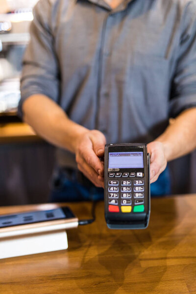 Young man barista giving payment service for customer with credit card and smiling while working at the bar counter in coffee shop.