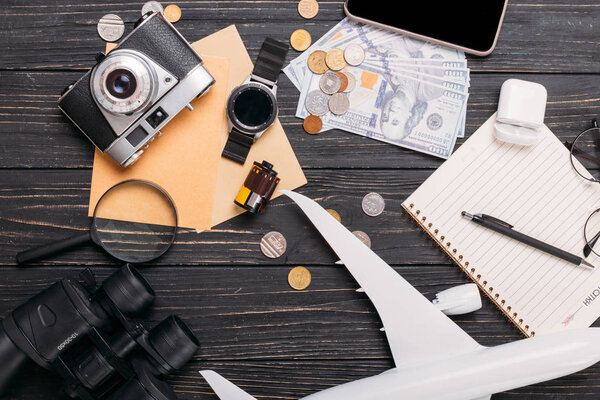 Travel concept on wooden table. Phone camera, money, plane and other accesories on desk.