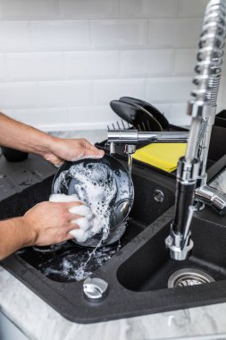 Adam el ile mutfakta bulaşık yıkar. Adam bir kirli tabak ve çamaşır sünger elinde tutuyor. Elle bulaşık yıkama kavramı.