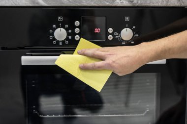 Kauçuk koruyucu temizlik ve Lehçe tencere elinde genç adam. Siyah parlak yüzey mutfak üst, eller, deterjan. Set temizlik kavramı