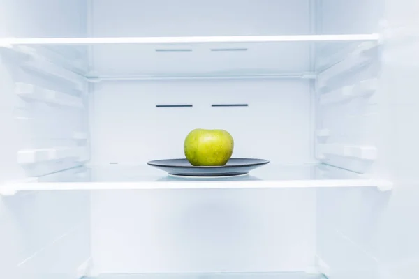 One green apple in open empty refrigerator. Weight loss diet concept.