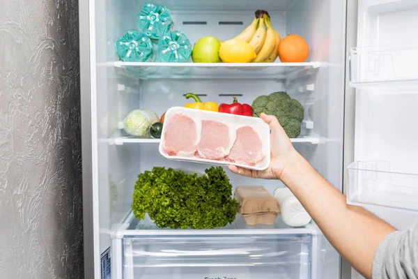 Hands take meat standing next to the open fridge. Food.