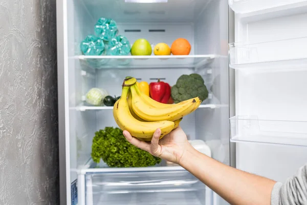 Mano elegir plátano de friedge completo. concepto de alimentación saludable — Foto de Stock