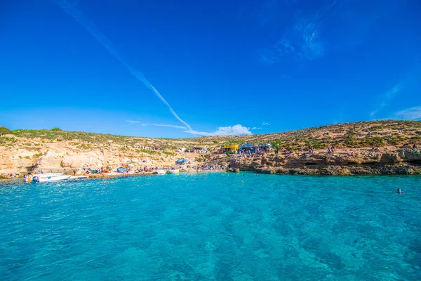 Comino, Malta - Noviembre, 2018: Turistas se congregan en Blue Lagoon para disfrutar del agua turquesa en un día soleado de verano con cielo azul claro y barcos en la isla de Comino, Malta . — Foto de Stock