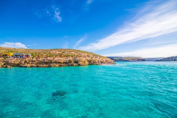 Comino, Malta - Noviembre, 2018: Turistas se congregan en Blue Lagoon para disfrutar del agua turquesa en un día soleado de verano con cielo azul claro y barcos en la isla de Comino, Malta . — Foto de Stock