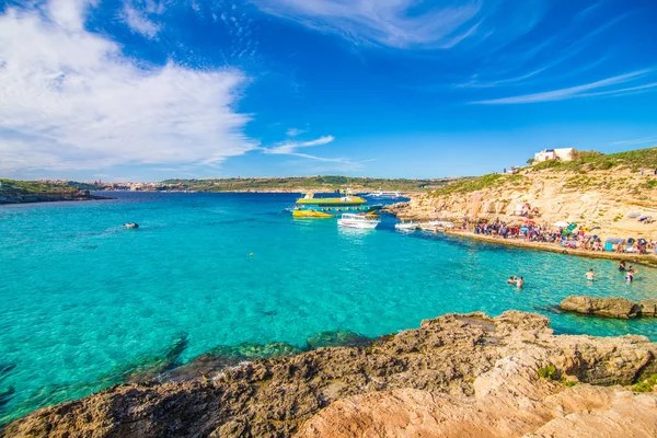 Comino, Malta - Noviembre, 2018: Turistas se congregan en Blue Lagoon para disfrutar del agua turquesa en un día soleado de verano con cielo azul claro y barcos en la isla de Comino, Malta . — Foto de Stock