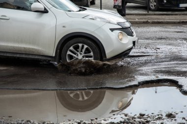 Araba çukurlar ve çukurlarda asfalt ile kötü bir yolda hızı azaltmadan gider, bir su birikintisi tekerlek isabet, her yöne eritme su püskürtme